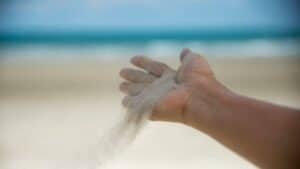 Close-up of hand releasing sand on sandy beach with ocean in background.