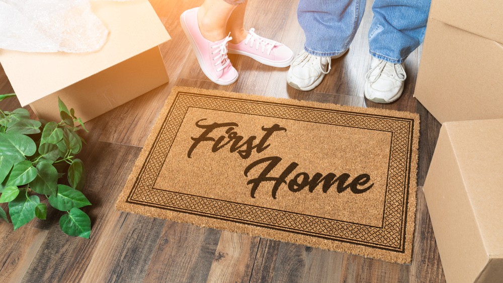 Man and Woman Unpacking Near Our First Time Buyer Welcome Mat, Moving Boxes and Plant.