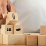 Person stacking wooden blocks with icons of a rocket, group, and chat.