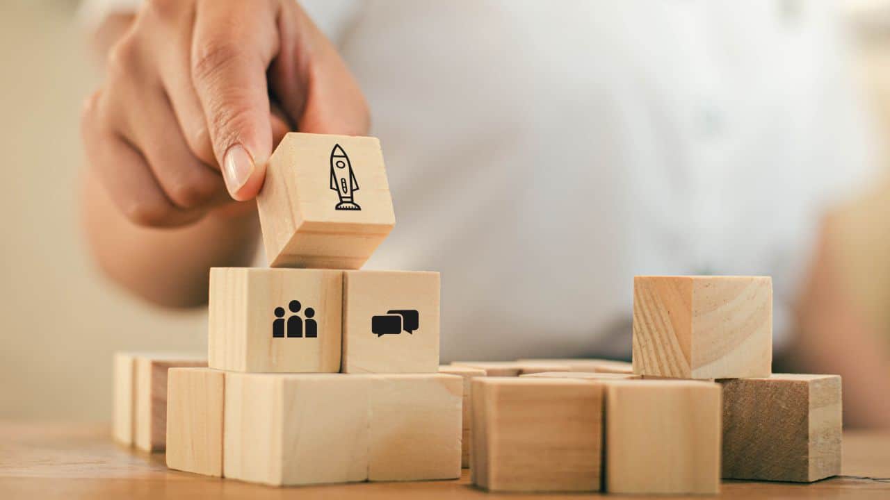 Person stacking wooden blocks with icons of a rocket, group, and chat.