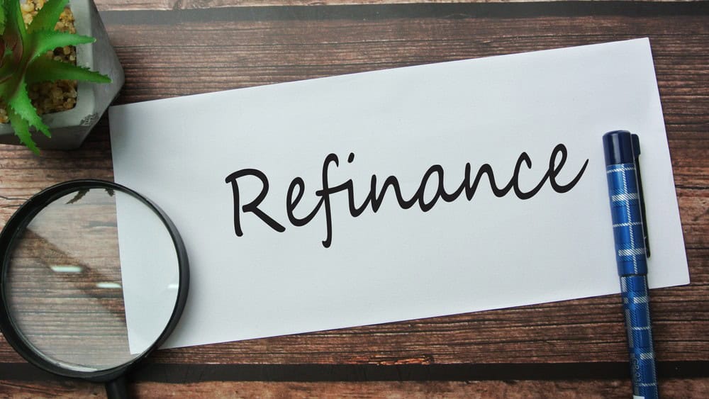Selective focus of magnify glasses, pen, flower and notebook written with REFINANCE.