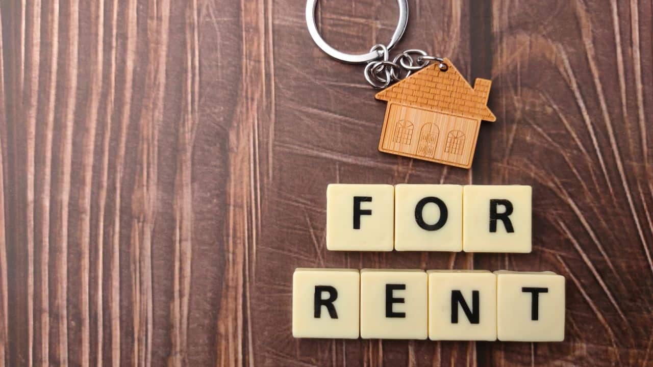 Keychain with house charm and 'For Rent' tiles on wooden surface.