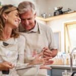 Cooking, love and food with a senior couple baking in the kitchen of their retirement home together. Romance, affection and bake with an elderly man and woman pensioner preparing a meal in the house