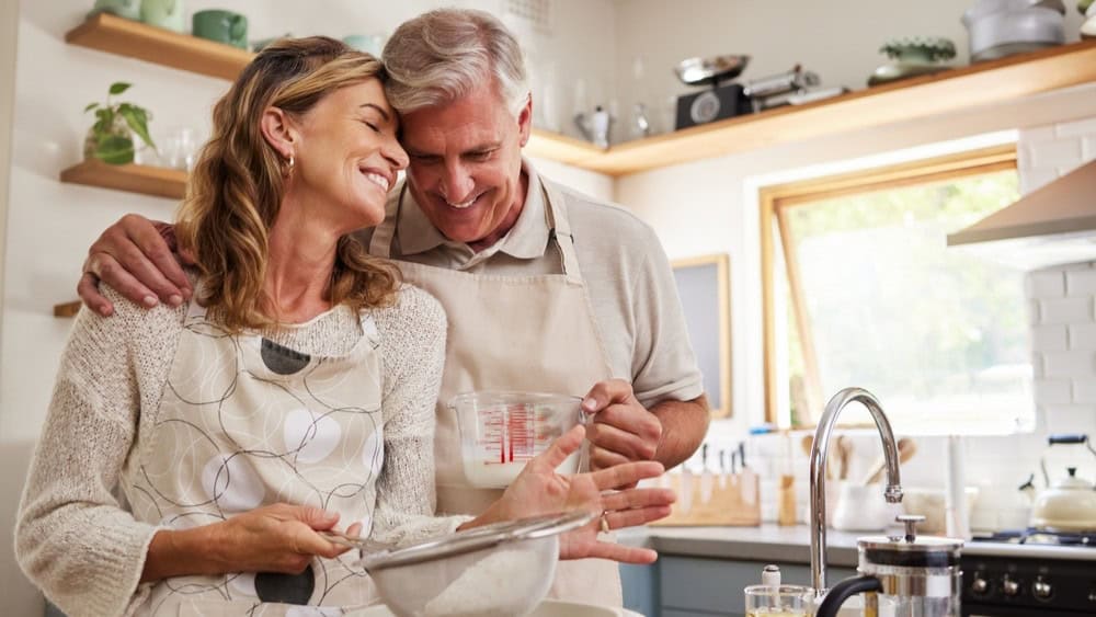 Cooking, love and food with a senior couple baking in the kitchen of their retirement home together. Romance, affection and bake with an elderly man and woman pensioner preparing a meal in the house