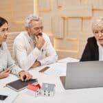 happy middle aged married couple looking at female realtor showing project of new home on laptop