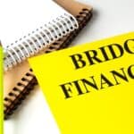Yellow folder with words bridge financing next to notebooks and pencil on white background .