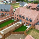 Aerial view of newly completed terraced houses showing installed heat pumps and lush green lawns. The new housing development is located in rural Britain.