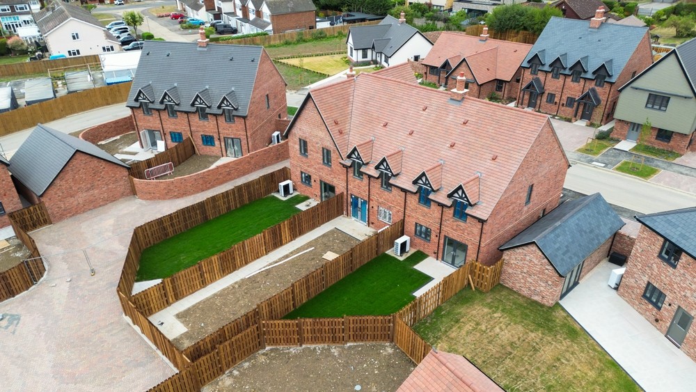 Aerial view of newly completed terraced houses showing installed heat pumps and lush green lawns. The new housing development is located in rural Britain.