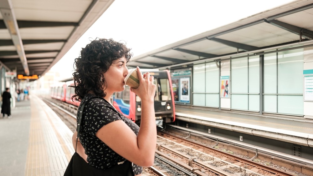 Young female commuter drinking coffee while waiting for the tube to arrive at a london underground station, enjoying a hot beverage during her daily commute